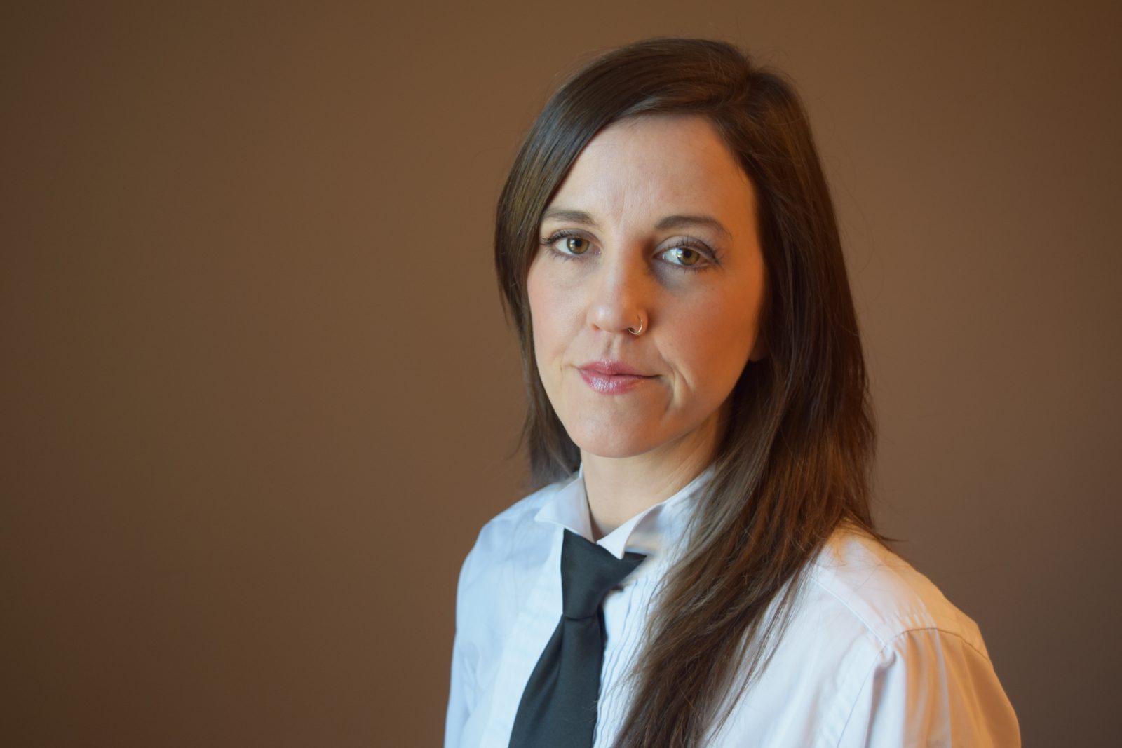 Prof. Stacy Douglas in a tie and white dress shirt, against a medium brown background