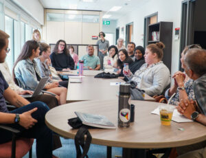 A full house event hosted in the Migration and Diasporas Studies Lounge listens as an attendee introduces herself.