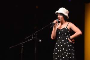 Alma in a polka dot dress and white hat sings with attitude