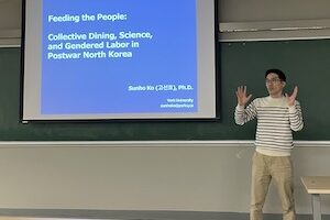 Professor Sunho Ko stands in front of a PPT with the words 