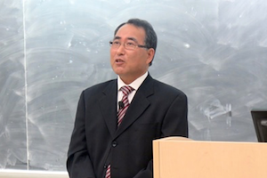 Dr. Takehiro Kanaya speaking on a stage