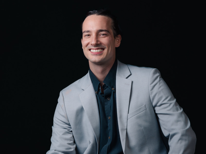 Dallas sitting comfortably in a suit with his hands on his knees