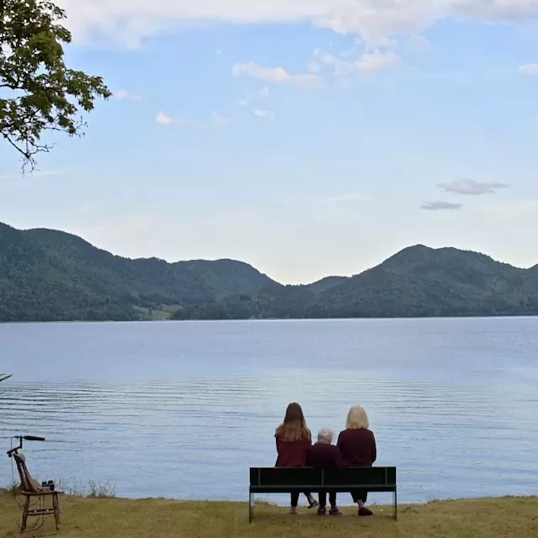 Three women on a bench looking out at a lake.