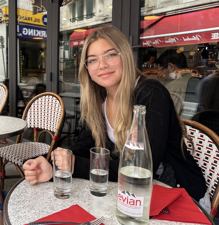 Josefina sitting at a cafe. Glasses of Evian water are on the table.