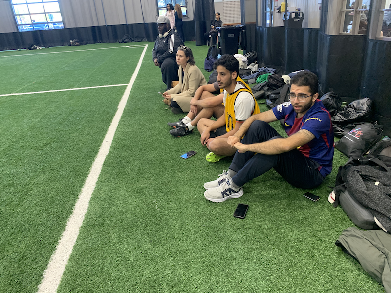 Julie and students sit on sidelines watching the game.