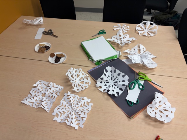 Paper snowflakes on a table with scissors and plates of cookies