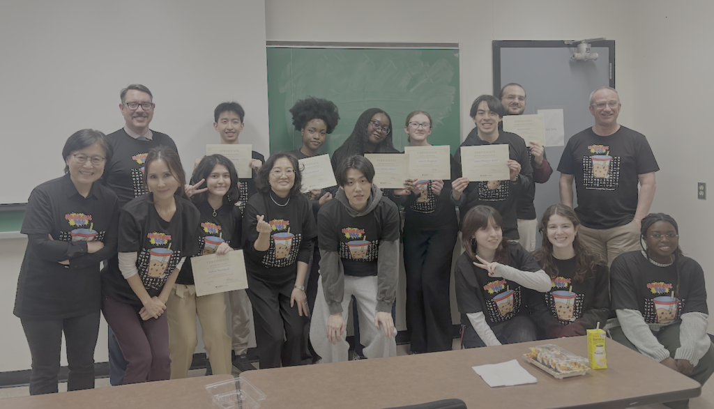 Group of students gathered at the front of the room...all wearing Korean teeshirts. Some holding certificates.