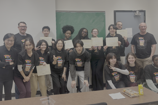 Group of students gathered at the front of the room...all wearing Korean teeshirts. Some holding certificates.
