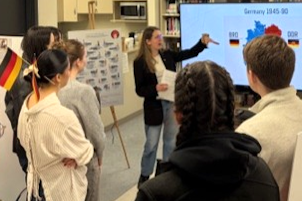 Group of students gathered to listen to rep from Embassy of Germany. PowerPoint shown on smart TV.