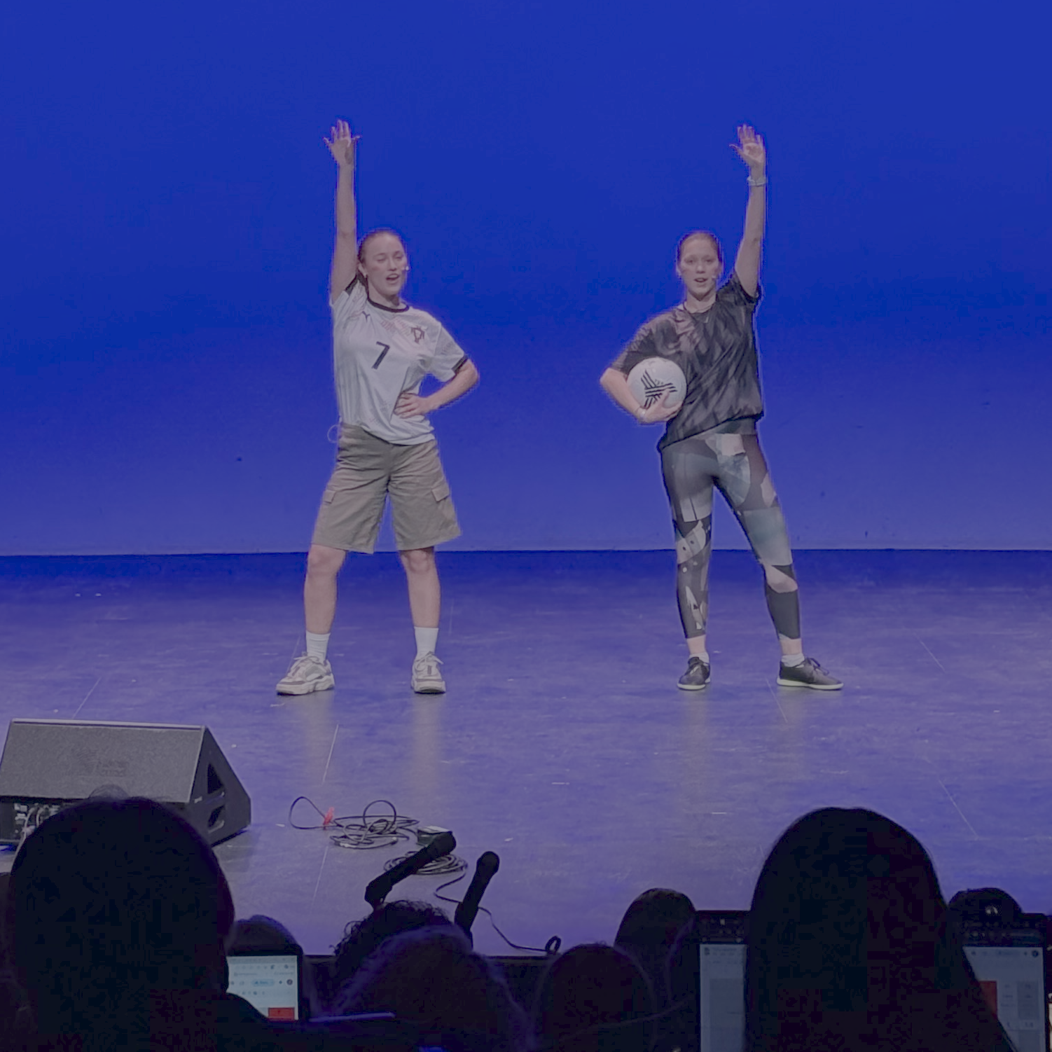 Stef and Alex at the end of their performance, hands raised, soccer ball in hand.