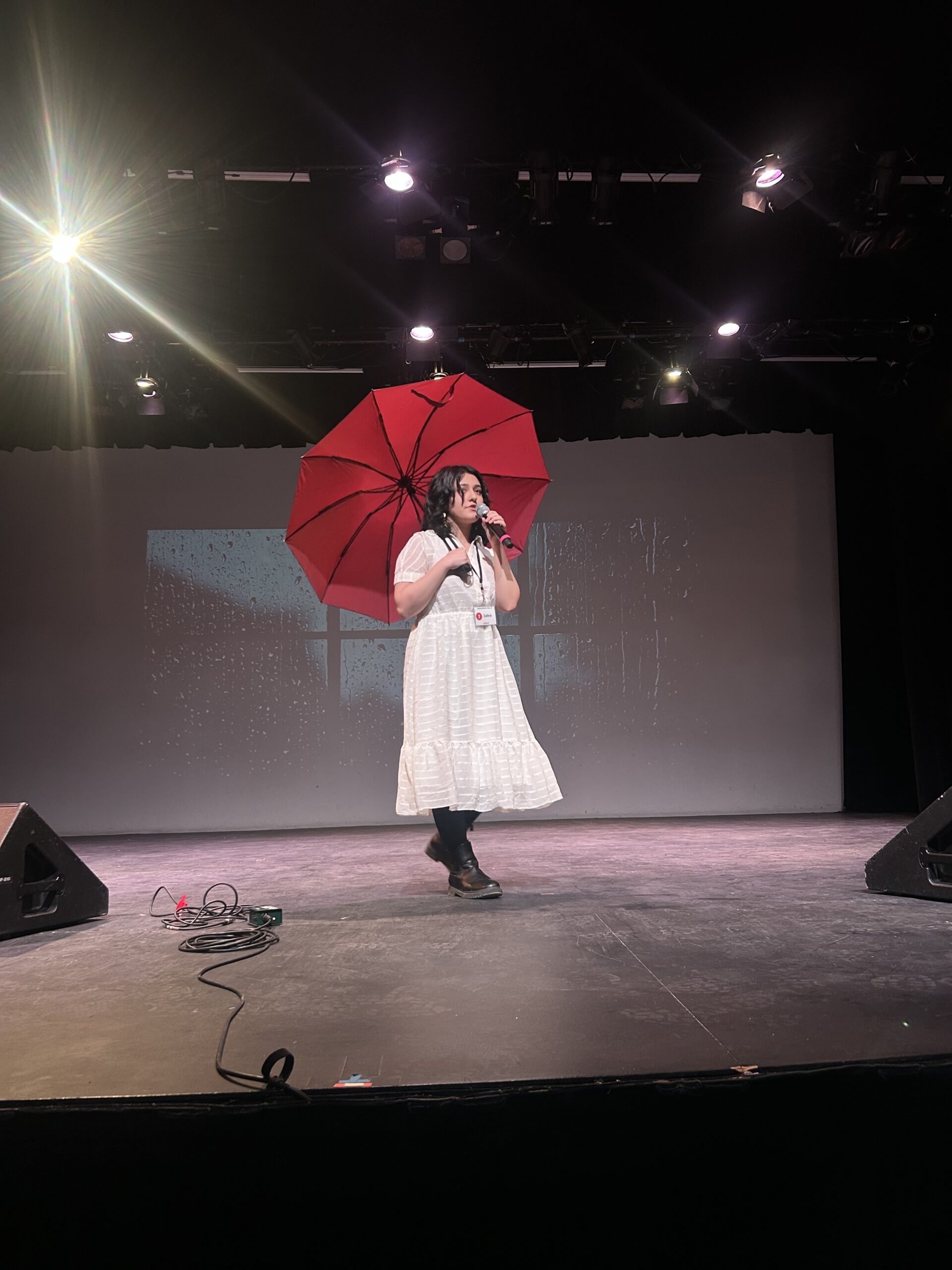Zahra with a red umbrella. Behind her, rain falls on a window pane.