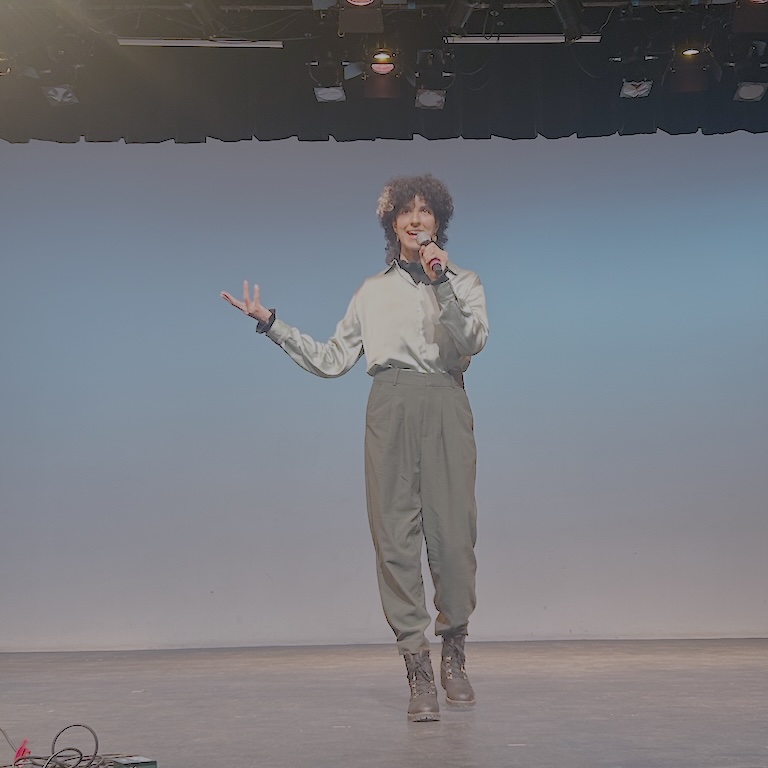 Alex walks confidently toward the front of the stage, microphone in hand.