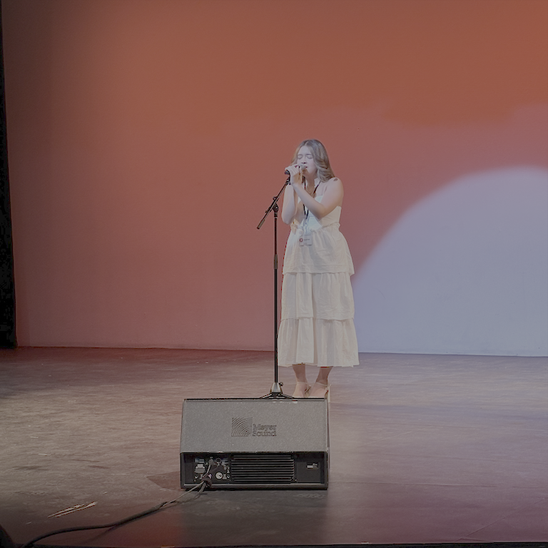 Sophie singing against a red background with a spotlight like a rising sun.