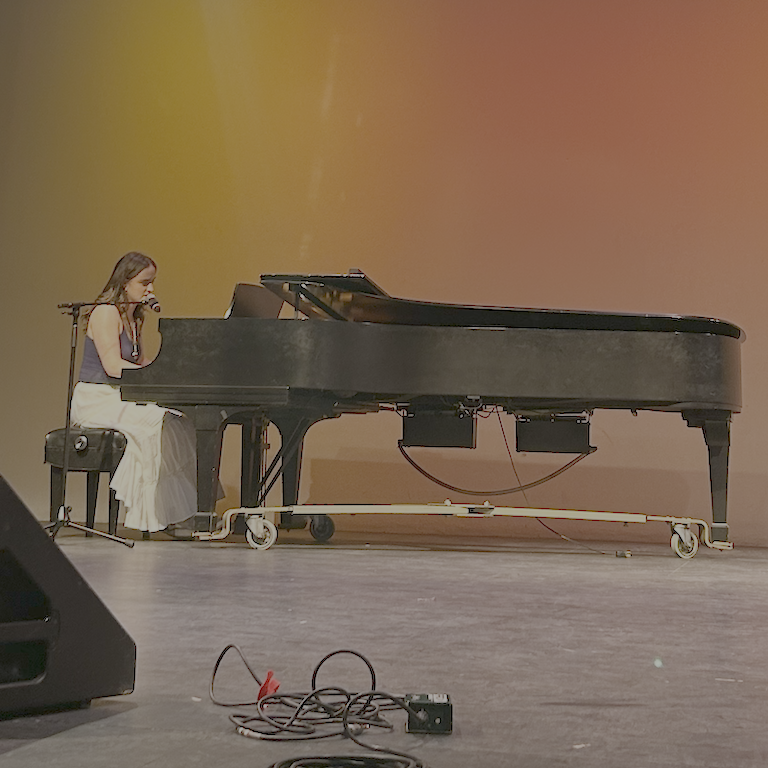 Lucy seated at the piano against an orange gold backdrop.