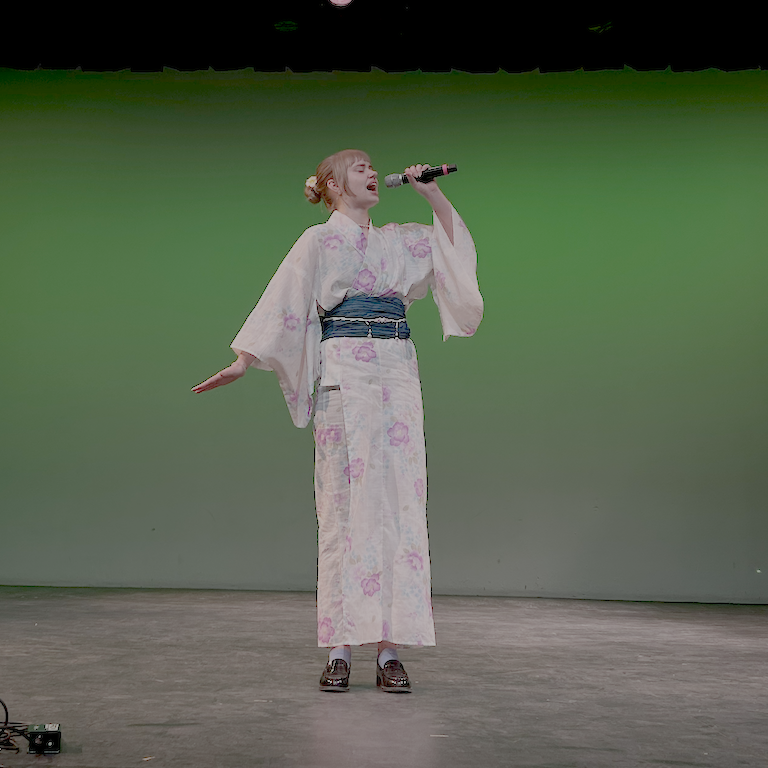 Serena dressed in a pink flower kimono belts out  her song.