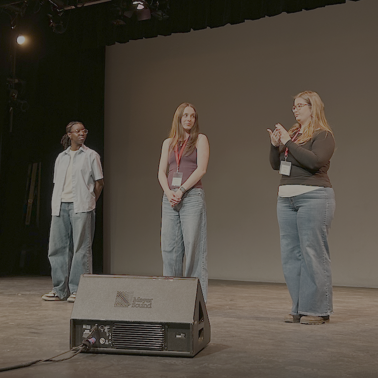 Three students signing to each other on a stage.
