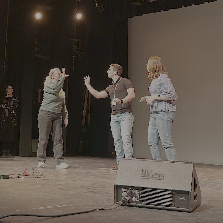 Two students appear to be having a conflict.  Sign to one another.  Another performer looks on.