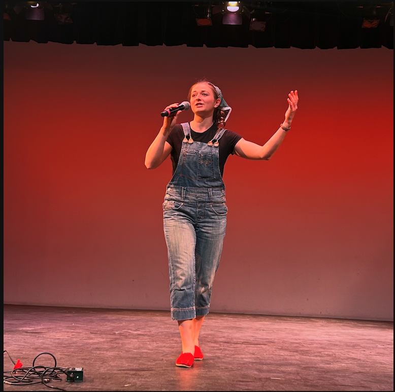 Chloé dressed in denim overalls, a bandana, and red shoes raises her hand urging people to join in.