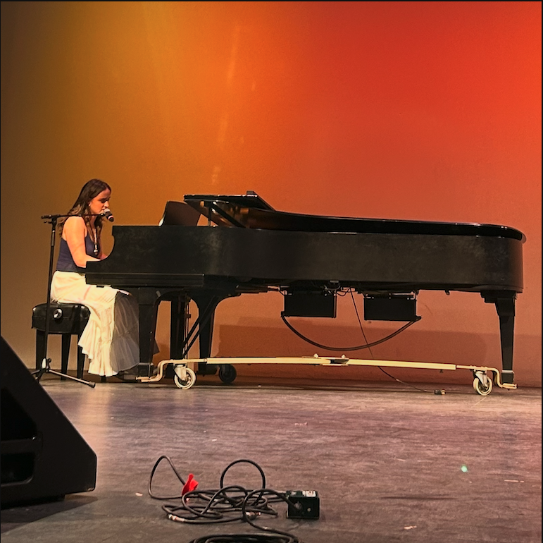 Lucy seated at the piano against an orange gold backdrop.