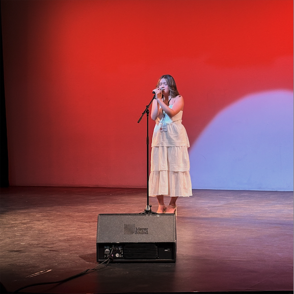 Sophie singing against a red background with a spotlight like a rising sun.