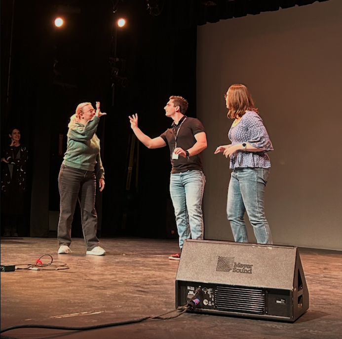 Two students appear to be having a conflict.  Sign to one another.  Another performer looks on.