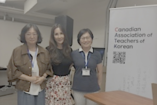 Seunghee, HJ, and Soyoung smile for the camera in front of the conference sign.
