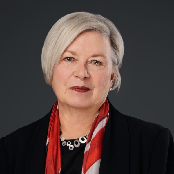 Susan Philips, a woman, wears a red, silk scarf, necklace and black jackets as she smiles at the camera.