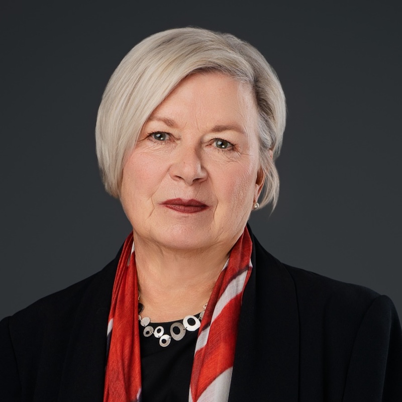 Susan Philips, a woman, wears a red, silk scarf, necklace and black jackets as she smiles at the camera.