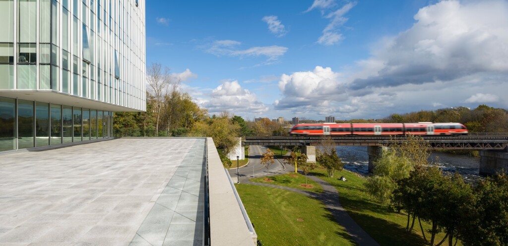 Photo of Richcraft Hall balcony and a train near a river, at Carleton University, Ottawa.