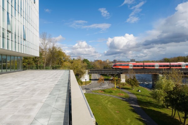 Photo of Richcraft Hall balcony and a train near a river, at Carleton University, Ottawa.