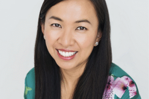A woman with a turquoise and pink dress and long, straight black hair smiles at the camera.