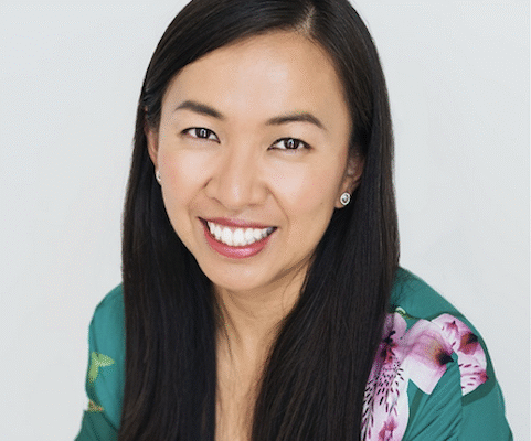 A woman with a turquoise and pink dress and long, straight black hair smiles at the camera.