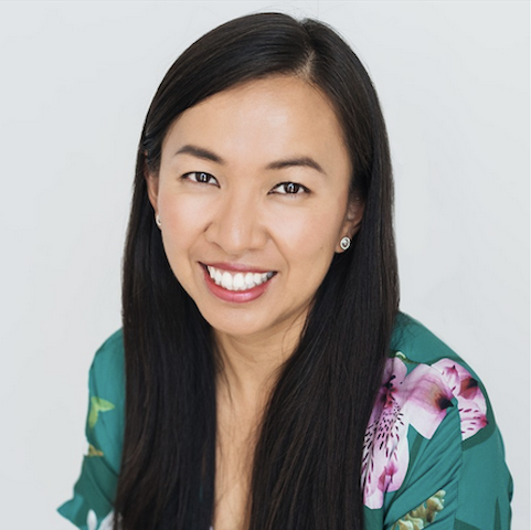 A woman with a turquoise and pink dress and long, straight black hair smiles at the camera.