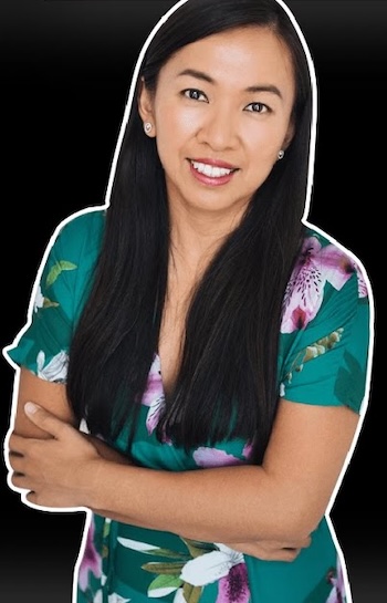A woman with long, straight black hair wearing a green dress with pink flowers smiles at the camera.