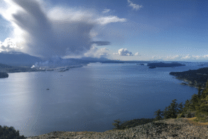 From the top of a mountain in British Columbia, we see a massive, white cloud dipping down to a huge lake.