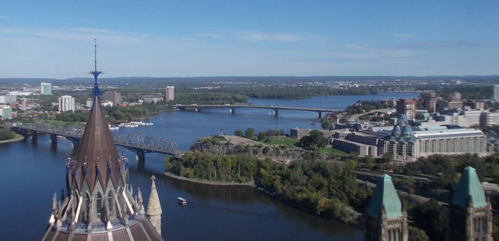 An aerial view from the top of Peace Tower at Parliament Hill, in Ottawa, with a panorama of the horizon, trees and two, long bridges crossing the Ottawa River.