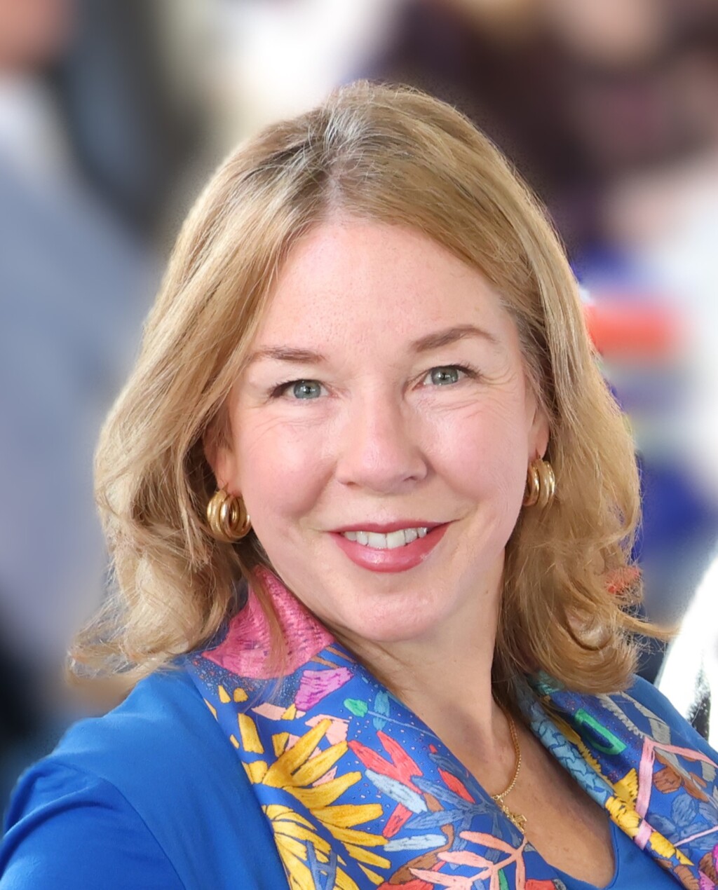 A woman, Rebecca Murray, wears a scarf and earrings and smiles at the camera.