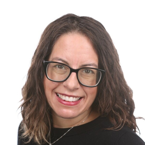A woman with long hair and glasses smiles at the camera.