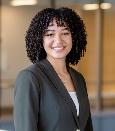 A woman (Karlee) with curly black hair and a blazer smiles at the camera.
