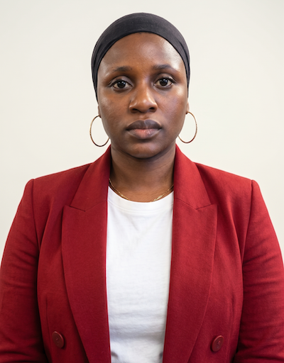 A woman (Olayinka) with a red jacket and hoop earrings looks at the camera.
