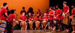 a group of students/people on a stage wearing red shirts and playing different instruments