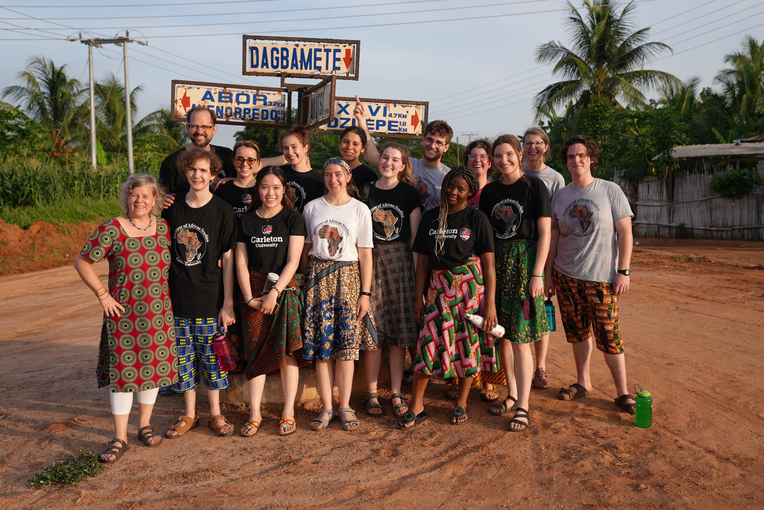 Group photo of Carleton students, faculty and staff in Ghana in front of Dagbamate village sign