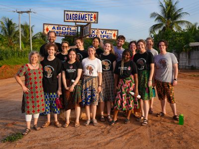 Group photo of Carleton students, faculty and staff in Ghana in front of Dagbamate village sign