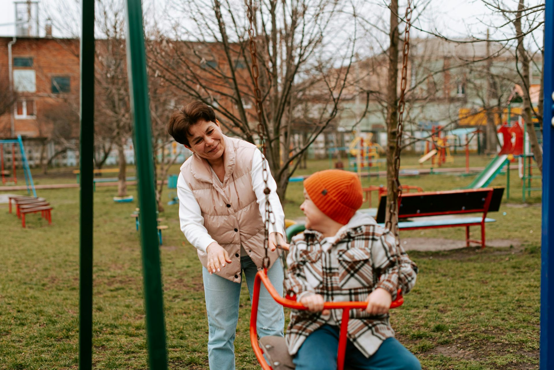 An older dark-haired woman plays with a boy at a playground, a visual representing parents and grandparents