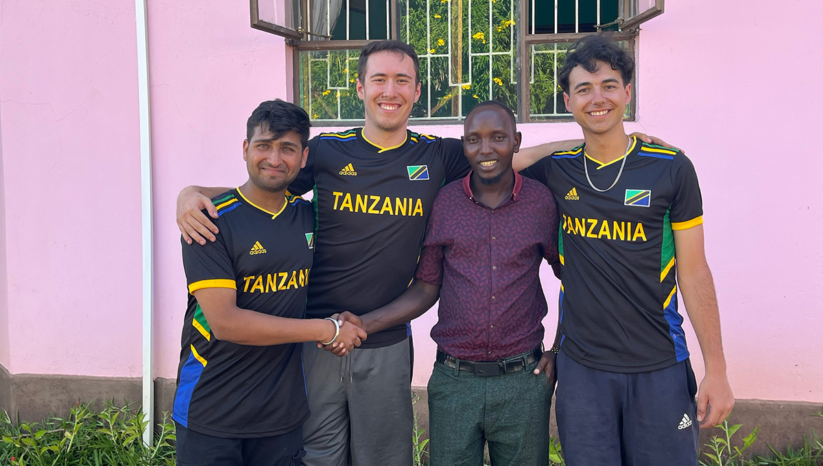 Four people posing for a group photo, with 3 of them wearing Tanzania soccer jerseys.