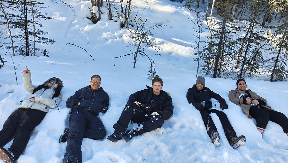 Five people smiling for the camera while laying in the snow.