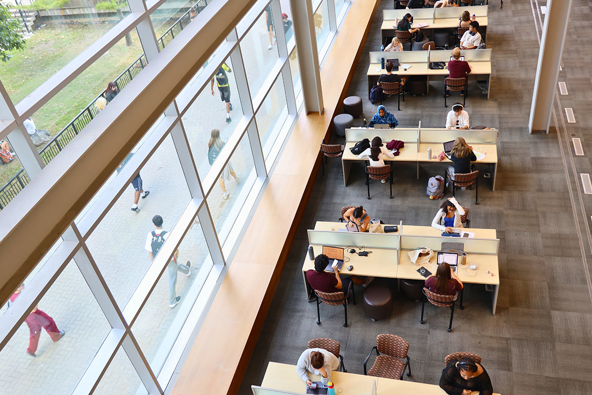 An aerial view of students sitting at large tables in a study hall.