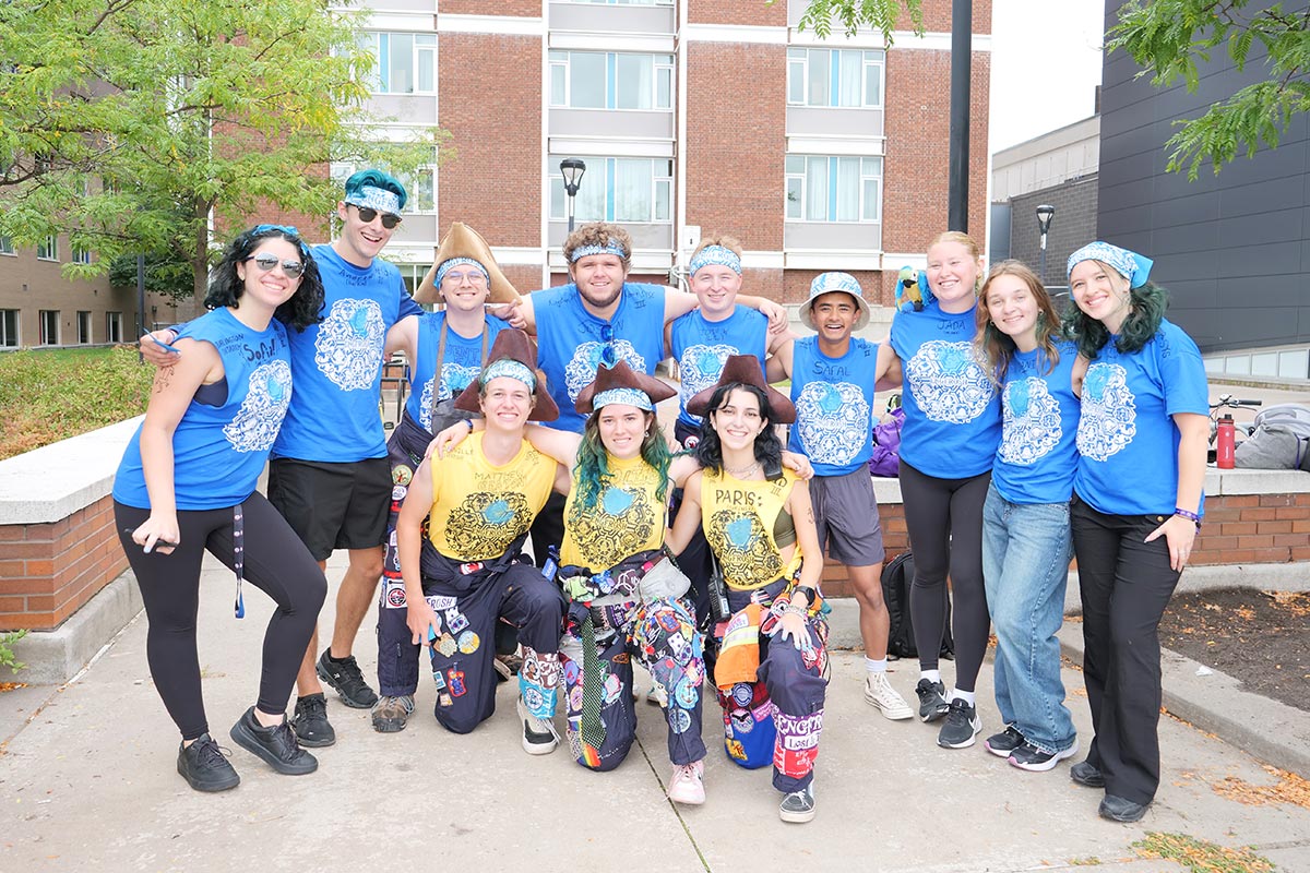 A large group of young adults wearing blue shirts pose for a photo outside of a brick building.