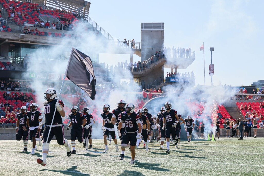 Carleton Ravens football players charge onto the field through smoke and flags during Panda Game.