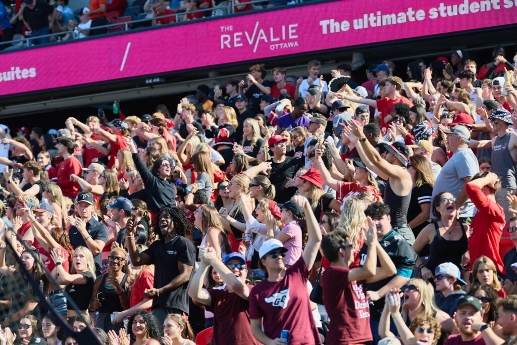 Excited fans wearing red and maroon cheer and wave in packed stands during the Panda Game between Carleton and uOttawa.